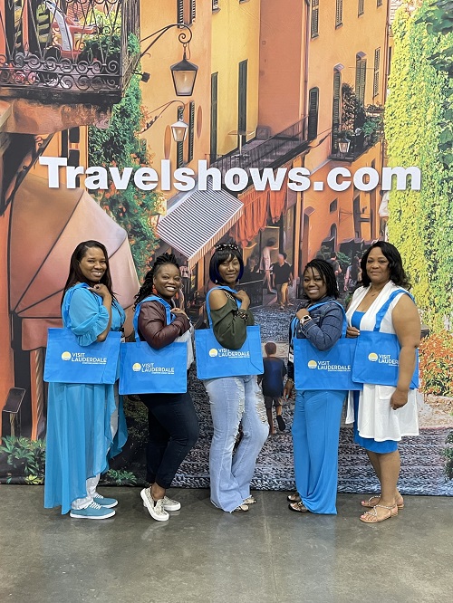 Five women posing with blue Visit Lauderdale bags in front of a mural 